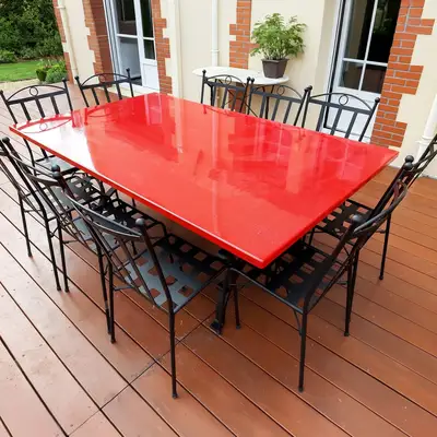 Glossy red rectangular lava stone table with iron chairs on a wooden terrace