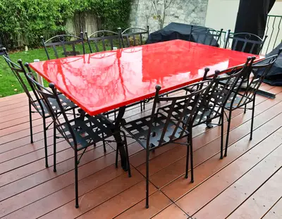 Rechteckiger roter Lavasteintisch mit schwarzen Stühlen, Ansicht der glänzenden Platte auf einer Holzterrasse.