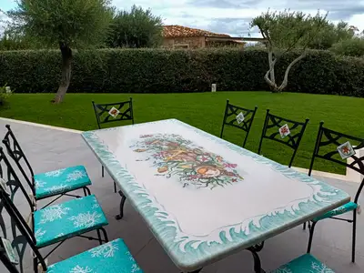 Lavasteintisch mit hellblauem Rankenrand und Eisenstühlen im Garten