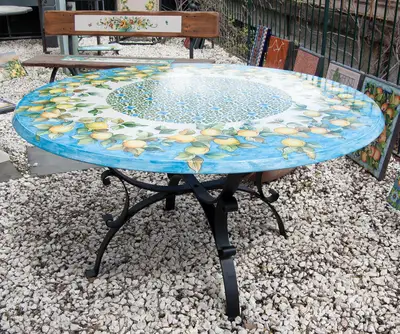 Round lava stone table with lemons on blue and an iron base, photographed outdoors on gravel.